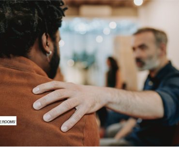 A man offers comfort by placing his hand on another man's shoulder during a conversation.