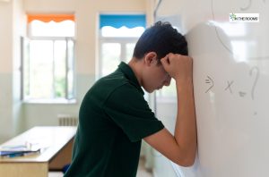 Stressed young boy leaning his head against a classroom whiteboard, symbolizing the impact of childhood struggles on future substance abuse risk.
