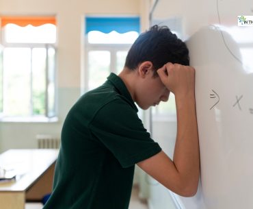 Stressed young boy leaning his head against a classroom whiteboard, symbolizing the impact of childhood struggles on future substance abuse risk.