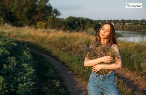 Woman standing outdoors on a dirt path, holding a bouquet of wildflowers with eyes closed, embracing peace and self-love.