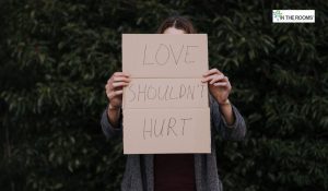 Person standing outdoors holding a cardboard sign that reads “LOVE SHOULDN’T HURT,” symbolizing emotional recovery and the courage to speak out against abuse.