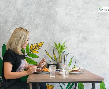 Woman sitting alone at a restaurant table, enjoying a meal and practicing self-care in recovery.
