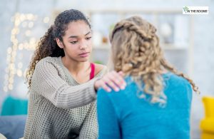 A young woman gently placing her hand on another person’s shoulder, offering comfort and support during an emotional moment.