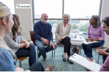 People sitting in a support group circle, smiling and sharing openly during a recovery meeting.