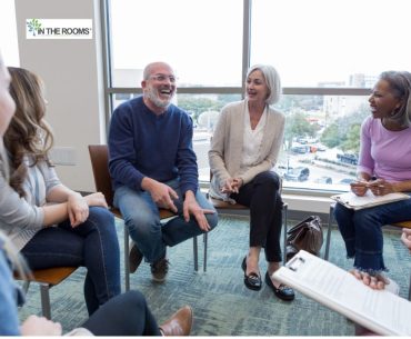 People sitting in a support group circle, smiling and sharing openly during a recovery meeting.