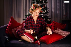 A woman sitting on a couch in holiday pajamas near a Christmas tree, holding a wine bottle and looking distressed, symbolizing emotional triggers and cravings during the holiday season.