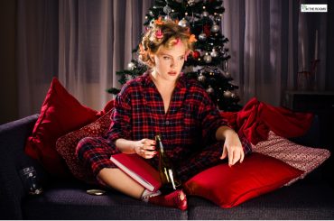 A woman sitting on a couch in holiday pajamas near a Christmas tree, holding a wine bottle and looking distressed, symbolizing emotional triggers and cravings during the holiday season.