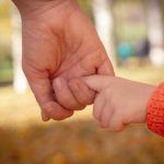 An adult holding a child’s finger during an outdoor walk, symbolizing trust, support, and emotional safety.