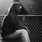 A person sitting alone on a bench, looking away thoughtfully in a quiet outdoor space, symbolizing reflection, guilt, and emotional healing in recovery.