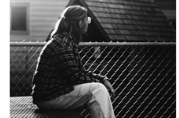 A person sitting alone on a bench, looking away thoughtfully in a quiet outdoor space, symbolizing reflection, guilt, and emotional healing in recovery.