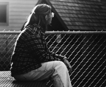 A person sitting alone on a bench, looking away thoughtfully in a quiet outdoor space, symbolizing reflection, guilt, and emotional healing in recovery.