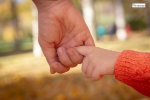 An adult holding a child’s finger during an outdoor walk, symbolizing trust, support, and emotional safety.