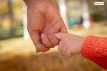 An adult holding a child’s finger during an outdoor walk, symbolizing trust, support, and emotional safety.