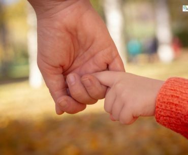 An adult holding a child’s finger during an outdoor walk, symbolizing trust, support, and emotional safety.
