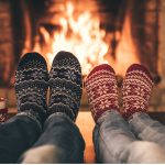 Two people in festive socks relaxing by a warm fireplace with mugs beside them, symbolizing calm, comfort, and a safe space during the holiday season.