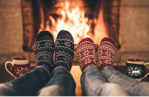 Two people in festive socks relaxing by a warm fireplace with mugs beside them, symbolizing calm, comfort, and a safe space during the holiday season.