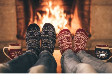 Two people in festive socks relaxing by a warm fireplace with mugs beside them, symbolizing calm, comfort, and a safe space during the holiday season.
