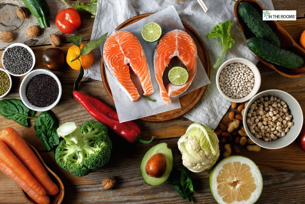 A balanced spread of whole foods including salmon, vegetables, fruits, legumes, and nuts, representing nutrition that supports healing and recovery.